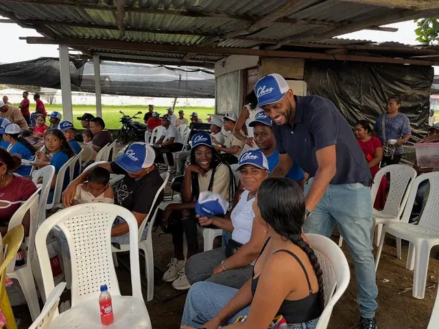 Personas sonrientes comparten una reunión comunitaria bajo un techo rural.