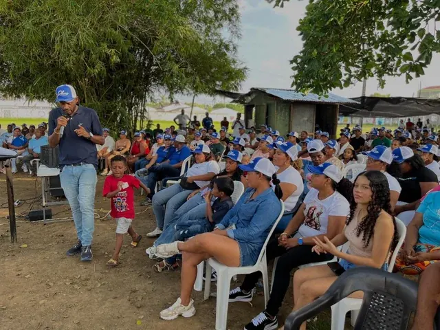 Encuentro al aire libre con una persona hablando por micrófono y familias sentadas.