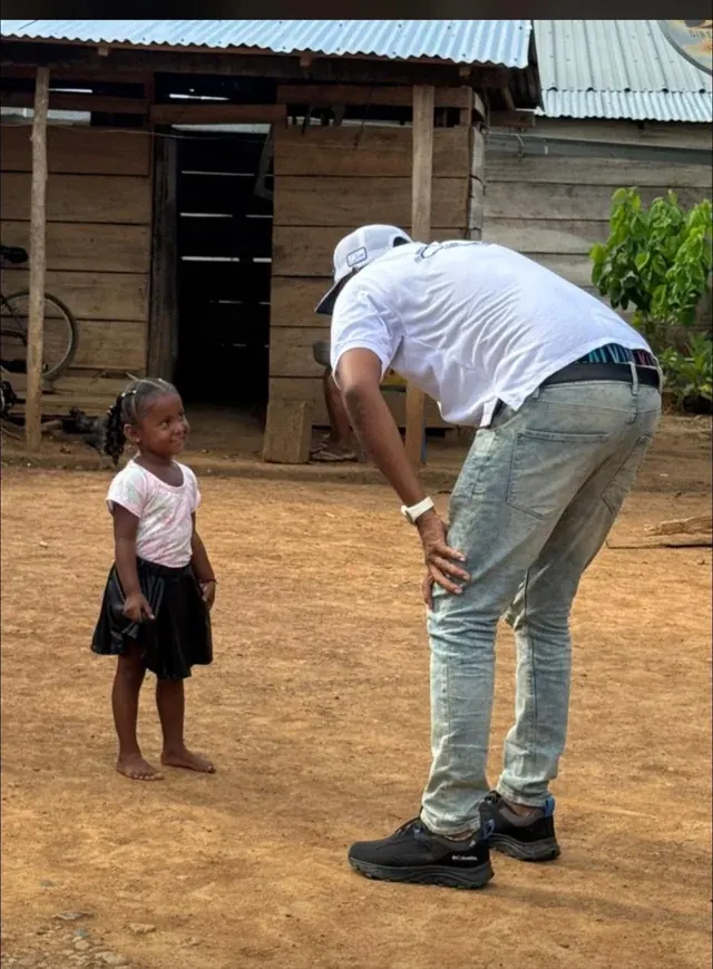 Una niña y un adulto comparten un momento frente a una vivienda de madera.